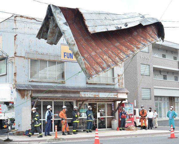 吹き飛ばされたトタン屋根の撤去作業に当たる消防隊員ら＝６日午前１０時２３分、松江市浜乃木４丁目